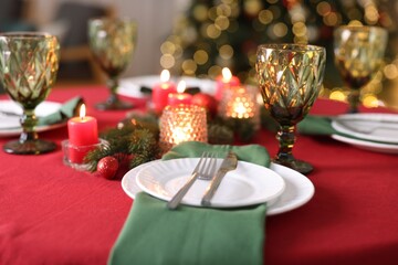 Stylish Christmas table setting with plates, glasses and burning candles in festive decorated room, closeup. Bokeh effect