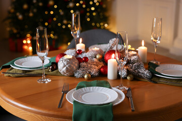 Stylish Christmas table setting with plates, glasses and burning candles in festive decorated room, closeup. Bokeh effect
