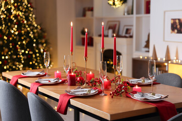 Stylish Christmas table setting with plates, glasses and burning candles in festive decorated room, closeup. Bokeh effect