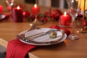 Christmas place setting with festive decor on wooden table in room, closeup