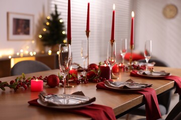 Stylish Christmas table setting with plates, glasses and burning candles in festive decorated room. Bokeh effect