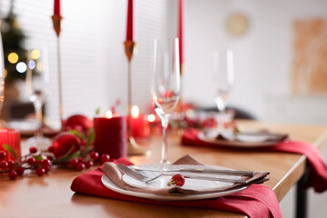 Stylish Christmas table setting with plates, glasses and burning candles in room, closeup. Bokeh effect