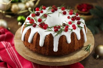 Delicious Christmas cake with icing, cranberries and rosemary on wooden table, closeup
