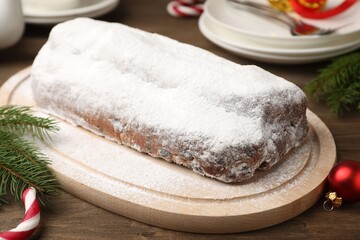 Traditional Christmas Stollen with icing sugar and festive decor on wooden table, closeup