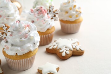 Tasty cupcakes with Christmas decor and gingerbread cookies on white table, closeup. Space for text