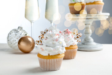 Tasty cupcakes with Christmas decor and champagne on white table, closeup. Bokeh effect