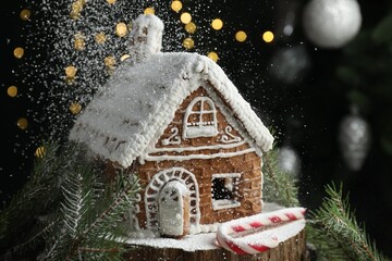 Powdered sugar as snow falling on gingerbread house against black background with blurred lights,...