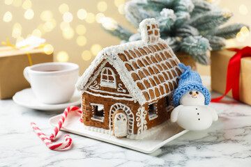 Gingerbread house and Christmas decor on white table against blurred lights