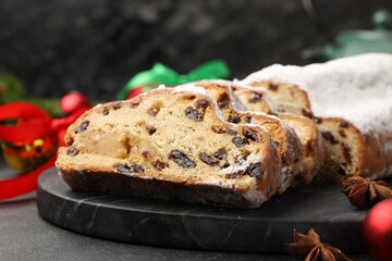 Traditional Christmas Stollen with icing sugar, spices and festive decor on black table, closeup