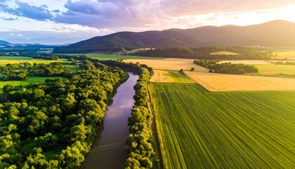 Aerial view of a verdant landscape with a river meandering through fields, lit by golden sunlight at sunset