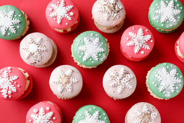 Beautifully decorated Christmas macarons on red background, flat lay