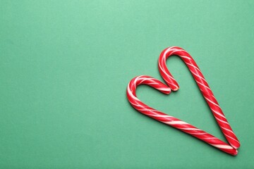 Fototapeta premium Heart made of candy canes on green background, top view with space for text. Merry Christmas and Happy New Year