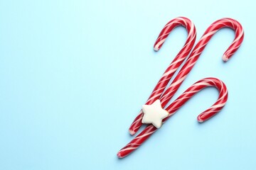 Tasty candy canes and gingerbread cookie on light blue background, flat lay with space for text. Merry Christmas and Happy New Year