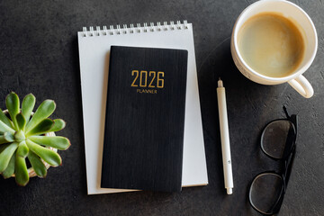 Stylish Desk Setup With 2026 Planner, Notebook, Pencil, Glasses, and Coffee on Wooden Surface