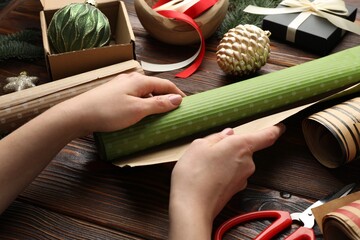 Festive packaging. Woman with gift box, ribbon, scissors, wrapping paper and Christmas decor at...