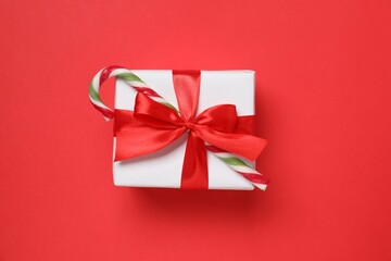Decorated Christmas gift with candy cane on red background, top view