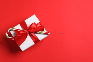 Decorated Christmas gift with candy cane on red background, top view. Space for text