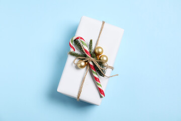 Decorated Christmas gift with candy cane on light blue background, top view