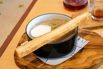 A bowl of creamy mushroom soup served on a wooden board, topped with a long piece of crispy garlic bread. Perfect for restaurant, culinary promotions, and cafe.