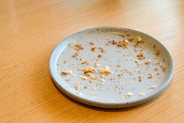 Top view of an empty gray ceramic plate with bread crumbs and food remains on a wooden table in natural light. Perfect for lifestyle blogs, restaurant ads, or food background designs