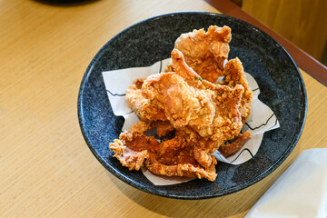 Crispy fried chicken skin served on a black ceramic bowl over a wooden table under natural light. Perfect for restaurant menus, snack product ads, or food blog illustrations