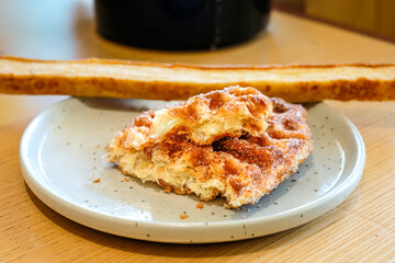 A croffle with cinnamon sugar topping and a slice of garlic bread served on a gray ceramic plate over a wooden table in natural light. Perfect for bakery advertising, cafe menu
