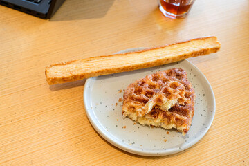 A croffle with cinnamon sugar topping and a slice of garlic bread served on a gray ceramic plate over a wooden table in natural light. Perfect for bakery advertising, cafe menu