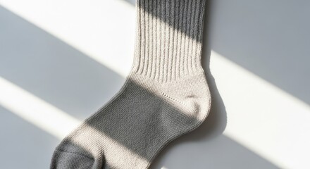 Single gray sock illuminated by sunlight on a white surface.