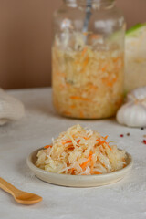 Fresh pickled cabbage, sauerkraut with carrot, garlic, and pepper on a light table with wooden spoon. Vertical orientation.
