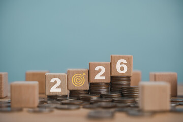 Wooden cube with the year 2026 on top of a stack of coins, symbolizing investment strategies,...
