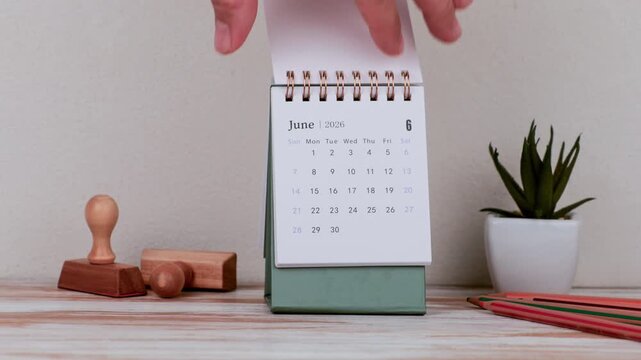 Hand Turning Desk Calendar to June 2026 on Workspace