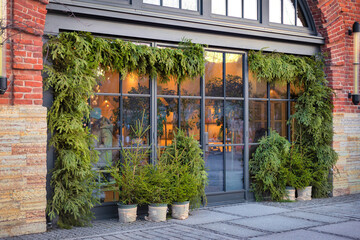 Garlands of fir branches and green spruce trees in front of a building on a city street. Festive street decor for the winter holidays.