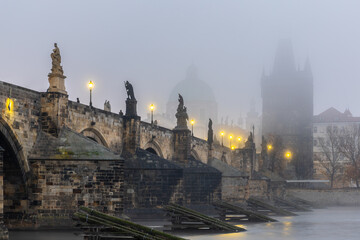 Charles Bridge over the Vltava River in Prague, Czech Republic, Shrouded in Morning Fog at Sunrise with Glowing Street Lamps, Empty of People, Creating a Calm and Atmospheric Cityscape