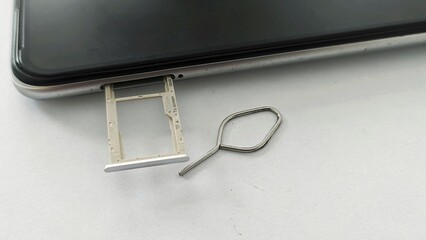 Top corner close-up of a mobile phone with a metallic ejector pin used to partially open the SIM card tray.