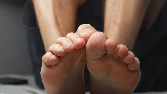 A close-up of a man's heels.
A barefoot man sits on a jivan.
A man wiggles his toes.
Toes, foot, leg, body, skin, barefoot
