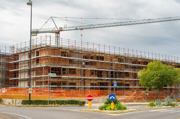 Construction of a brick residential building using red scaffolding and a tower crane. Equipment for building construction