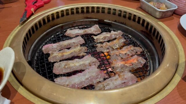 Thinly sliced marbled meat sizzling on a traditional Japanese yakiniku charcoal grill at a restaurant for a delicious barbecue dinner