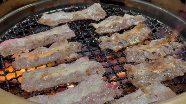 Close-up of delicious thin-sliced marbled beef sizzling on a traditional Japanese yakiniku barbecue over hot charcoal