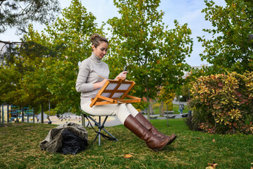 Woman painting on a portable easel with brushes in hand.