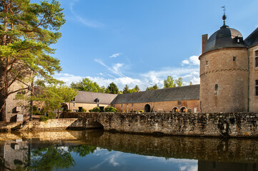 Château de Lavaux-Sainte-Anne reflected in calm waters under a clear blue sky in Belgium with its iconic round tower, stone bridge, and surrounding greenery capturing the essence of medieval European 