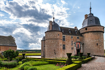 Château de Lavaux-Sainte-Anne stands majestically against a dramatic cloudy sky, surrounded by manicured gardens, stone towers, and the peaceful Belgian countryside evoking centuries of history 