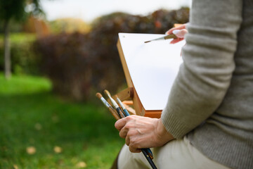 Close-up of artist painting on blank canvas outdoors.