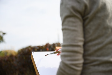 Close-up of artist painting on blank canvas outdoors.