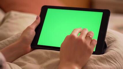 Closeup of a persons hands interacting with a green screen tablet swiping and tapping while relaxing on a bed or couch at home ideal for digital content display. - Powered by Adobe