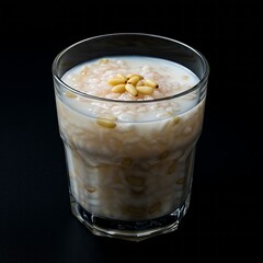 A glass of sikhye 식혜  (sweet rice punch) with floating rice and pine nuts, served in a black glass against a black background