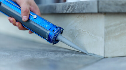 Applying sealant with a caulking gun to seal a gap between tiles