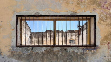 view through old window with rusty bars looking into building with no roof