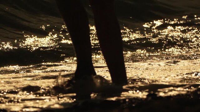 Feet beach water, person walking in shimmering golden water at sunset