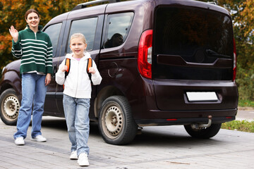 Mother taking her daughter to school near car outdoors
