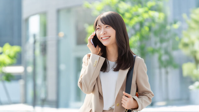 スマートフォンで通話しながら微笑むビジネスウーマン、屋外のオフィス街, Smiling businesswoman talking on a smartphone outdoors in an office district
